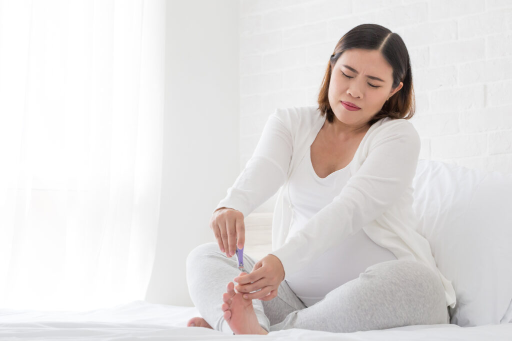 Pregnant woman cutting nails feet by nail clipper on white bed in the bedroom